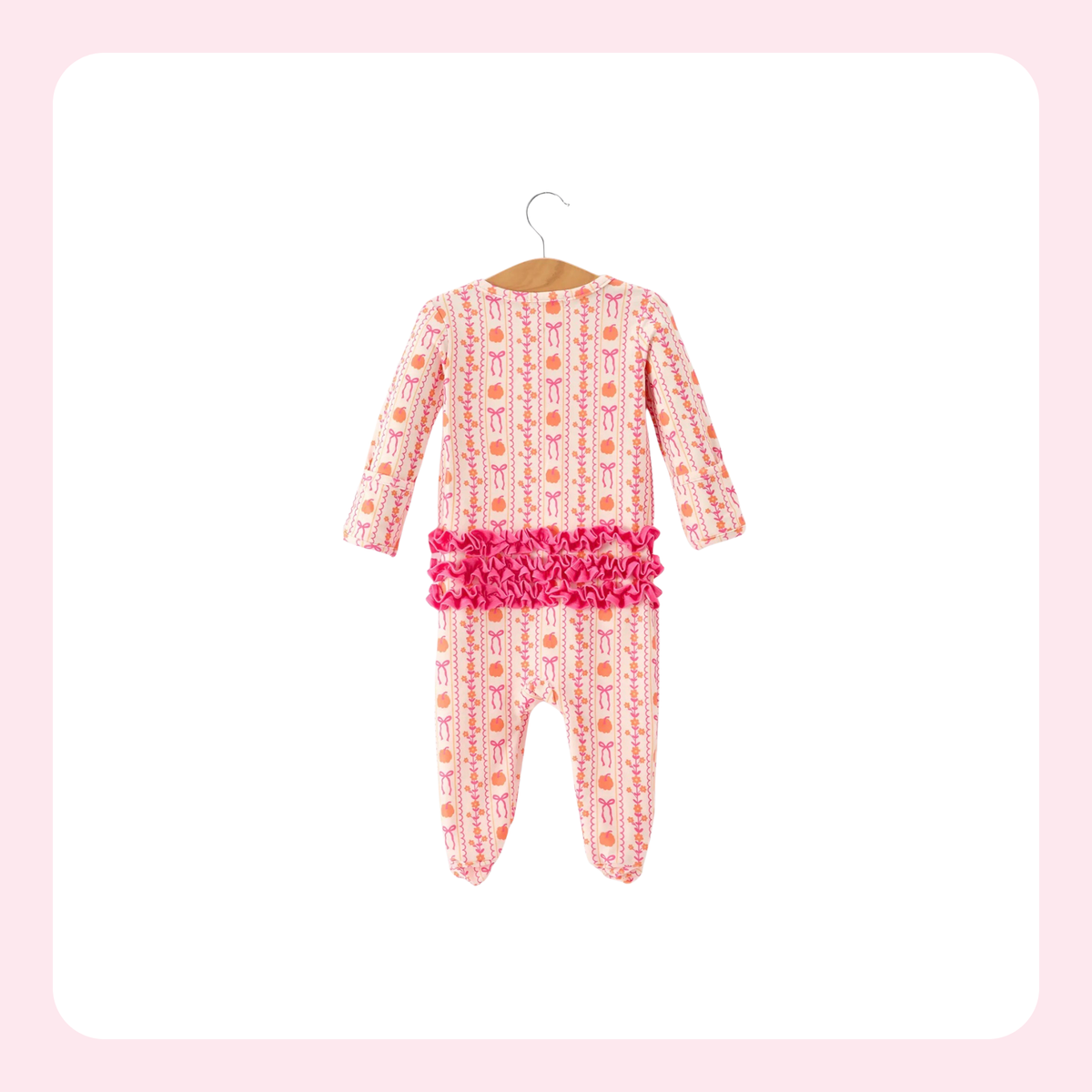 A baby long-sleeve footed one-piece jumpsuit in pink, featuring a vertical pattern of cartoon bunnies and orange carrots, with a prominent bright pink ruffled trim at the waist, shown hanging on a wooden hanger against a white background with a light pink border.