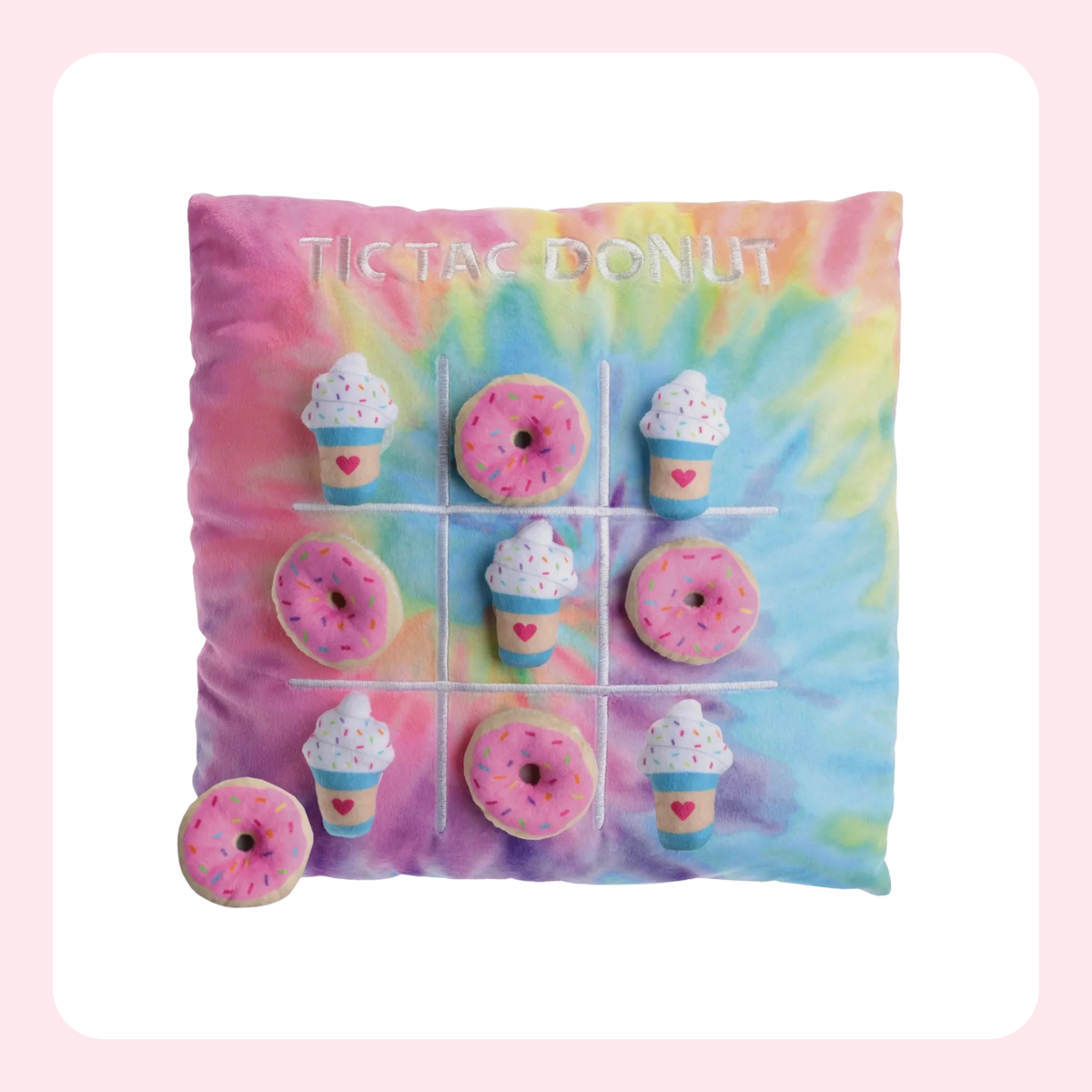 A square tie-dye pillow featuring a tic-tac-toe game design with donut and cupcake pieces, set against a light pink background.