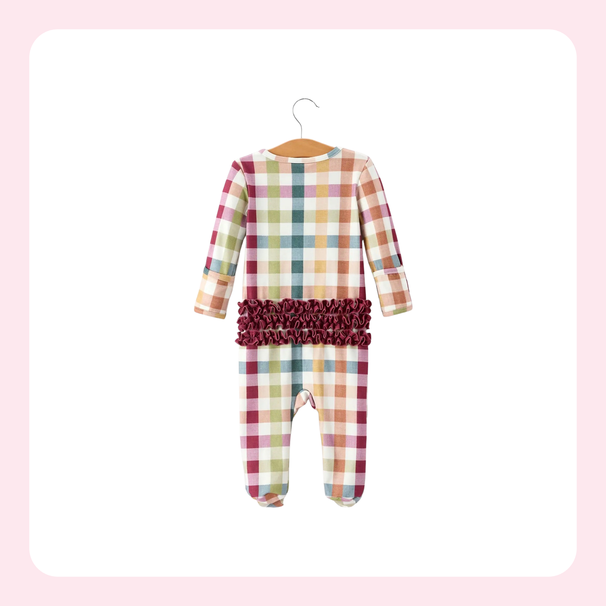A baby long-sleeve footed one-piece jumpsuit with a multicolor plaid pattern and a dark burgundy ruffled waistband, hanging on a wooden hanger against a white background with a soft pink border.