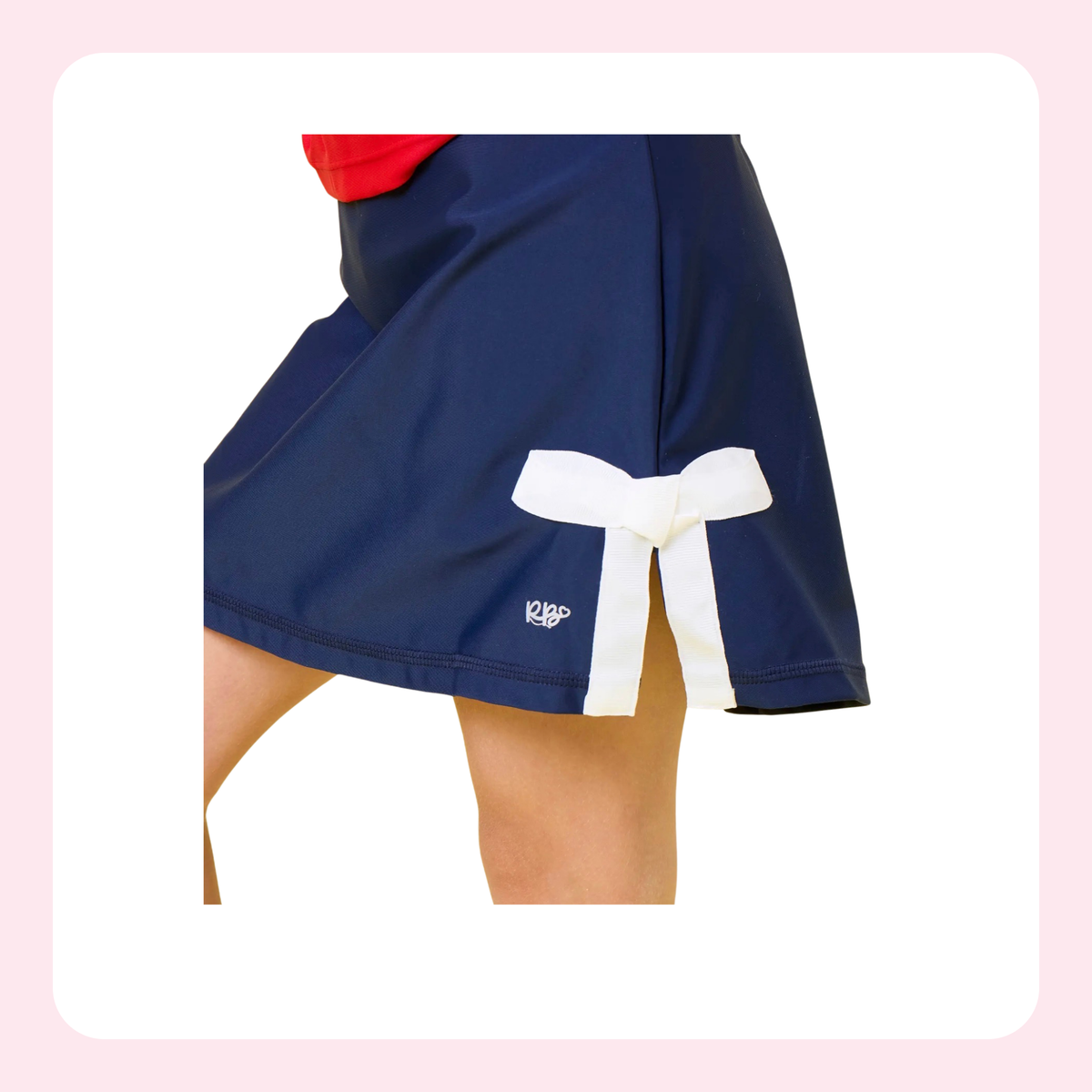 Close-up of a person wearing navy athletic shorts with a white side tab tied in a bow and a small white K1AP logo near the hem.