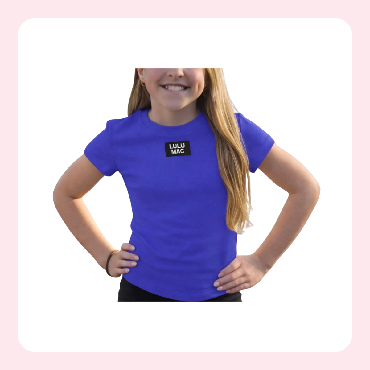 A young girl with long blonde hair wearing a bright blue short-sleeve t-shirt with a black chest logo that reads 'LULU MAC'. She is posing with her hands on her hips against a white background with a light pink border.
