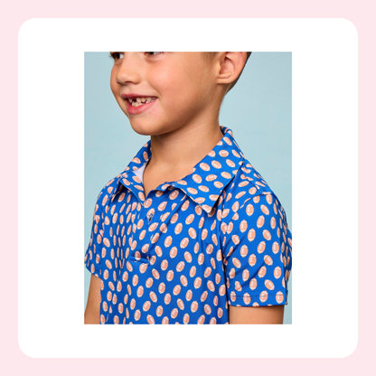 A young boy wearing a blue short-sleeve polo shirt with a pink and white pattern, shown in a side-profile portrait against a light blue background with a white and pink border.
