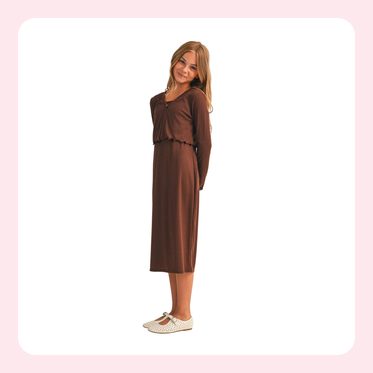 A woman modeling a brown long-sleeve midi dress with a gathered sweetheart neckline and a matching fabric belt, paired with white Mary Jane flats, set against a white background with a light pink border.
