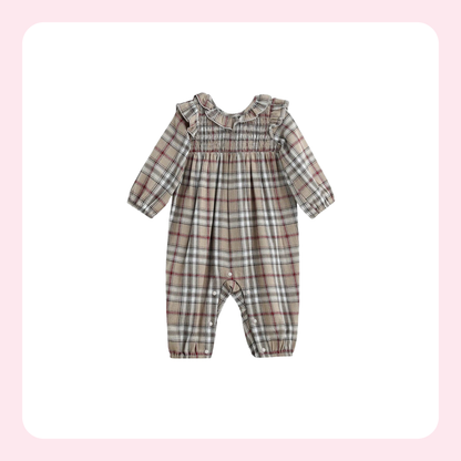 A baby long-sleeve romper in a beige, brown, and white plaid pattern, featuring a ruffled collar and elasticized leg cuffs, shown against a white background with a soft pink border.
