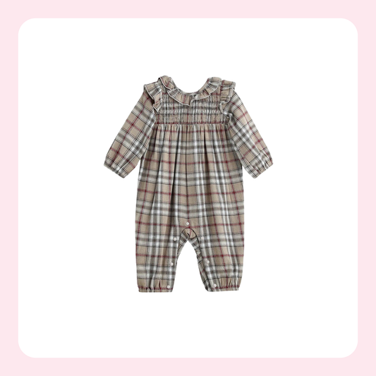 A baby long-sleeve romper in a beige, brown, and white plaid pattern, featuring a ruffled collar and elasticized leg cuffs, shown against a white background with a soft pink border.