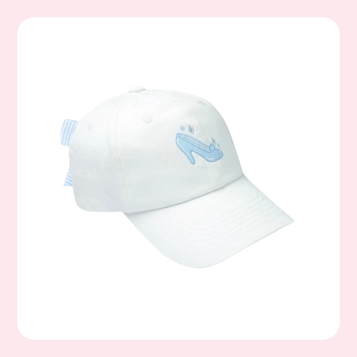 A white baseball cap featuring a light blue embroidered Cinderella's glass slipper on the front, with a matching light blue striped fabric tag on the side, set against a white background with a soft pink border.