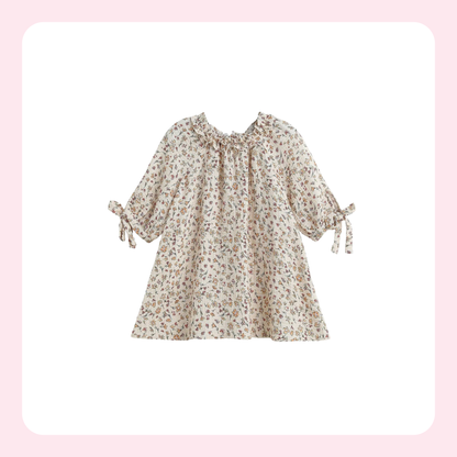 A cream-colored long-sleeve blouse with a small brown and beige floral print, featuring a ruffled neckline and tie details on the sleeves, shown against a white background with a soft pink border.