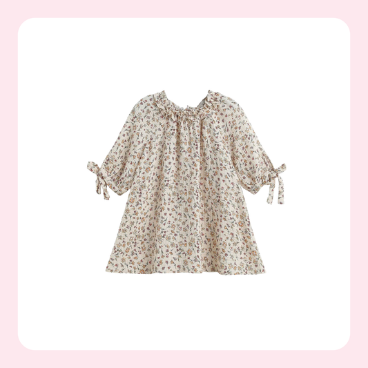 A cream-colored long-sleeve blouse with a small brown and beige floral print, featuring a ruffled neckline and tie details on the sleeves, shown against a white background with a soft pink border.