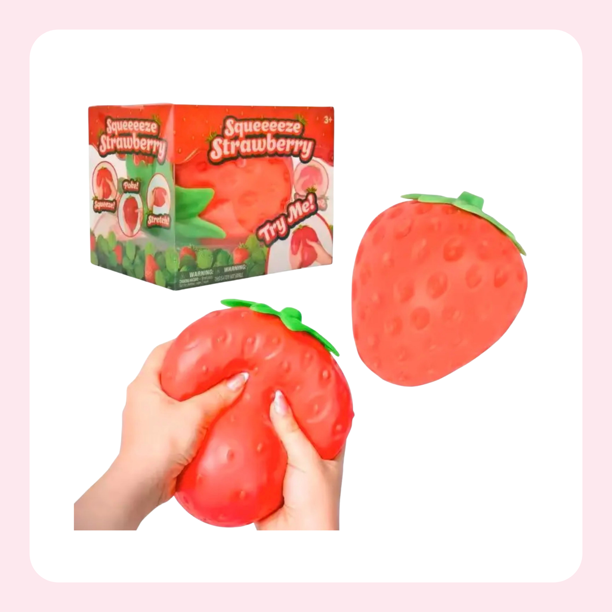 A strawberry-shaped squeeze toy shown with its retail box and being held by two hands. The product is bright red with a green leafy top and textured surface, set against a white background with a light pink border.