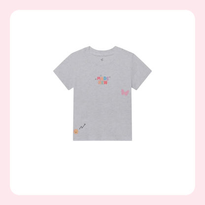 A light gray heather short-sleeve t-shirt with colorful graphic prints, including the text 'MADAME NEW' in pastel colors, a pink butterfly on the right chest, and a small yellow smiley face with a black squiggle on the bottom left hem, displayed on a white background with a soft pink border.