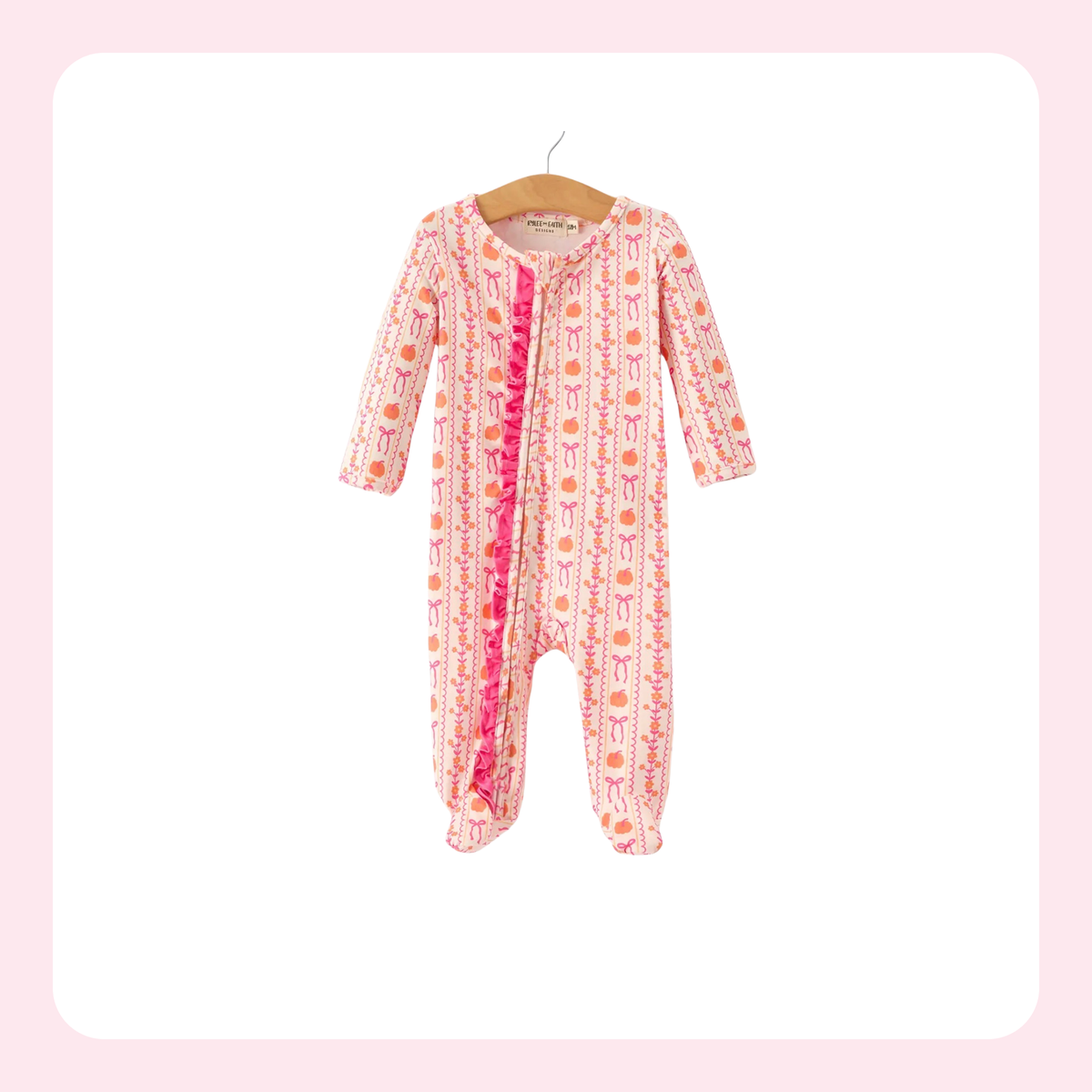 A baby footed sleeper with long sleeves and legs, featuring a pink and white patterned print with orange accents and a bright pink ruffle trim down the front, hanging on a wooden hanger against a white background with a light pink border.
