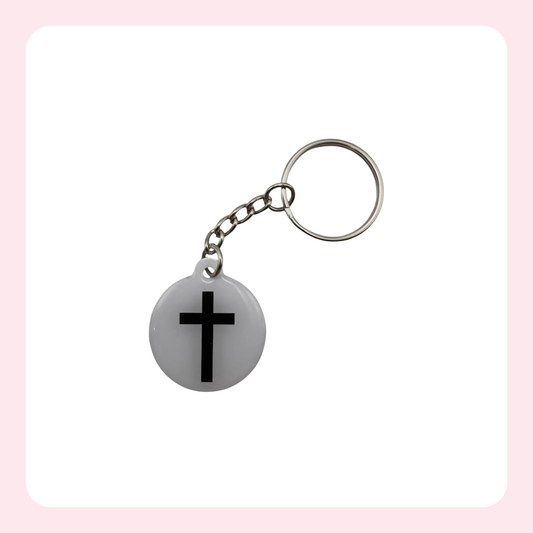 A silver metal keychain with a round white pendant featuring a black cross, set against a white background with a light pink border.