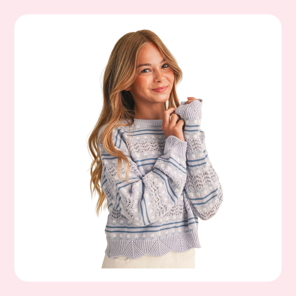A woman with long blonde hair wearing a light gray and blue patterned knit sweater, posing against a white background with a soft pink border.