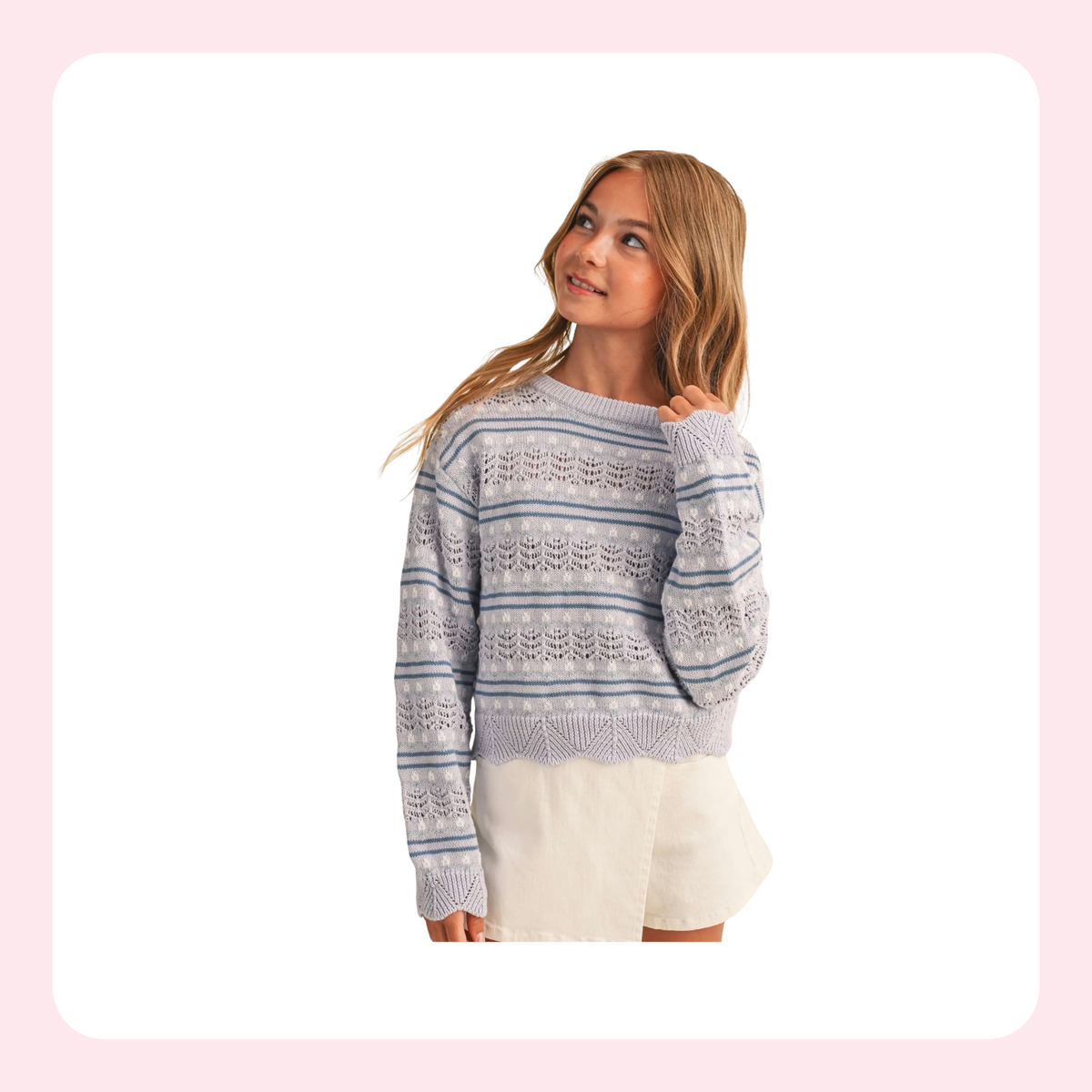 A young woman modeling a light blue and white patterned knit sweater with cream shorts against a white background with a soft pink border.