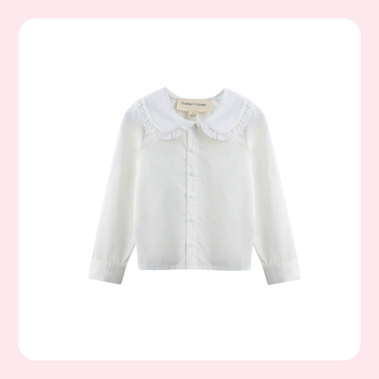 A white long-sleeve button-up blouse for toddlers, featuring a ruffled Peter Pan collar and a small button placket, shown against a white background with a light pink border.