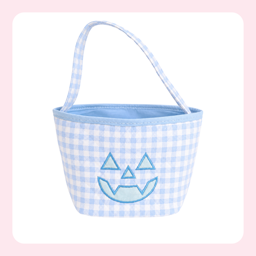 A small fabric bucket bag with a light blue and white gingham pattern, featuring a light blue embroidered jack-o'-lantern face on the front and a matching light blue handle, set against a white background with a soft pink border.