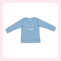 A light blue long-sleeve crewneck sweatshirt featuring a white embroidered jack-o'-lantern face on the front, displayed flat against a white background with a soft pink border.