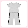 A two-piece kids' loungewear set in light heather gray, featuring a short-sleeve crewneck top and matching wide-leg pants. The set is accented with black side stripes on the pants and small black ribbon bows at the shoulder, sleeve, and pant leg edges.