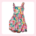 A sleeveless floral dress with ruffled shoulder straps and a gathered skirt, featuring a vibrant pink, green, yellow, and red floral pattern on a white background.