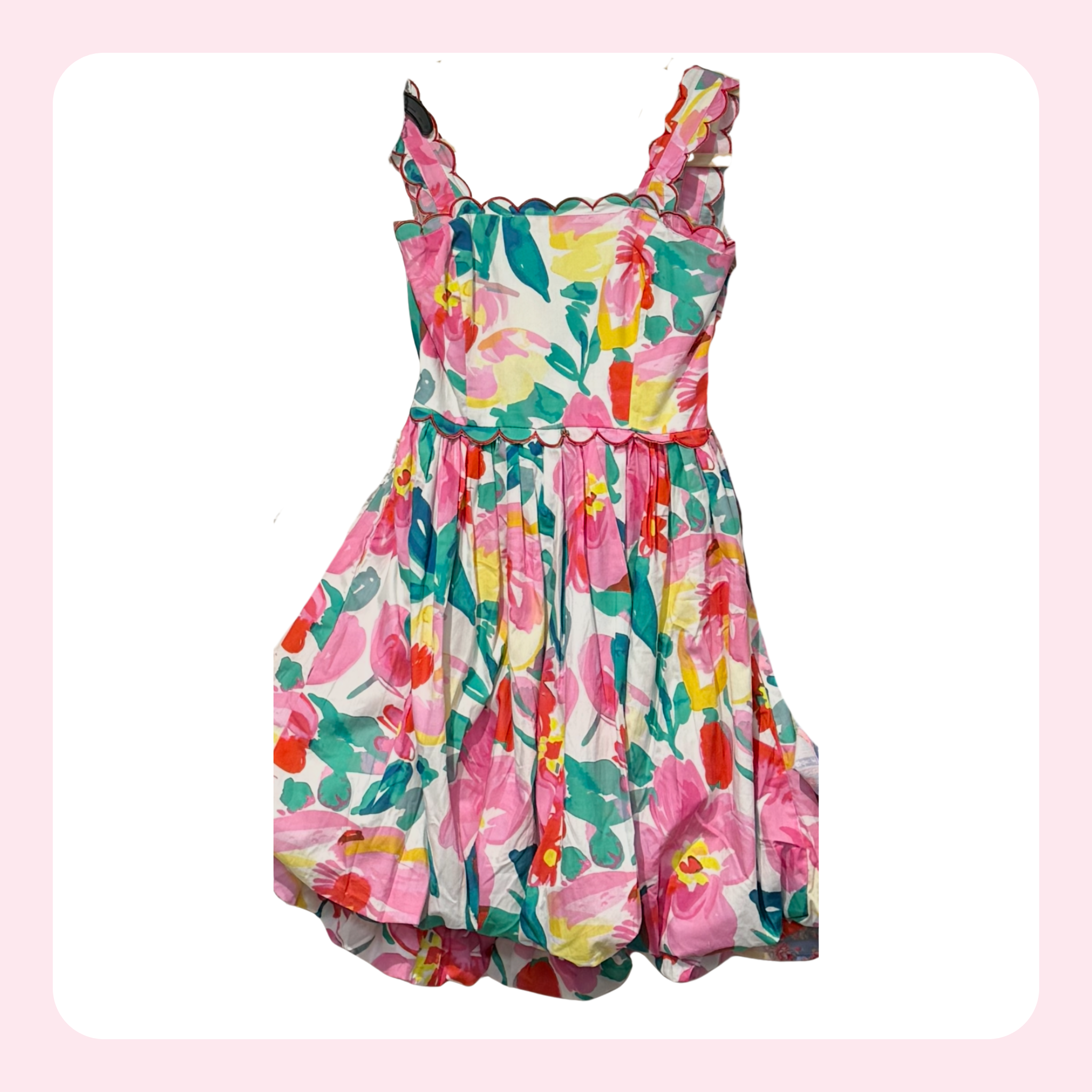 A sleeveless floral dress with ruffled shoulder straps and a gathered skirt, featuring a vibrant pink, green, yellow, and red floral pattern on a white background.