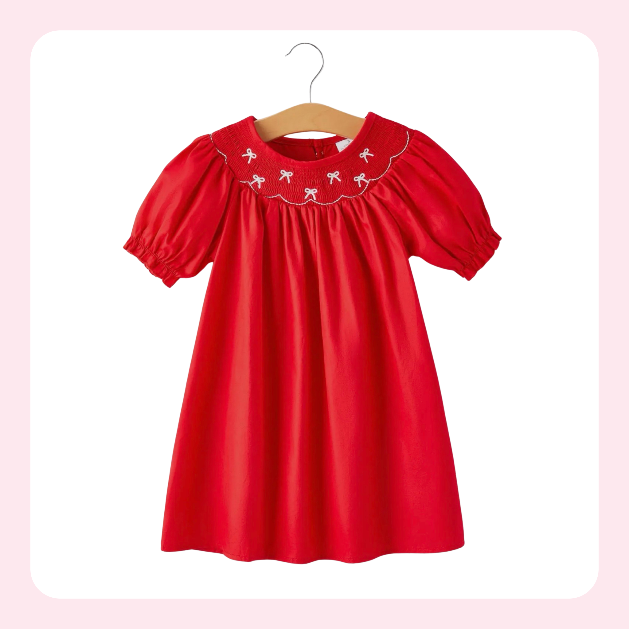 A bright red short-sleeve baby dress with puff sleeves and white embroidered flamingos on the yoke, hanging on a wooden hanger against a white background with a soft pink border.