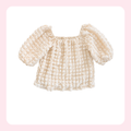 A cream-colored textured baby top with puff sleeves and a square neckline, displayed on a white background with a soft pink border.