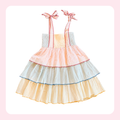 A pastel tiered babydoll dress with pink ribbon shoulder straps tied in bows, featuring layers of peach, pale blue, and cream ruffles with thin colored trim.