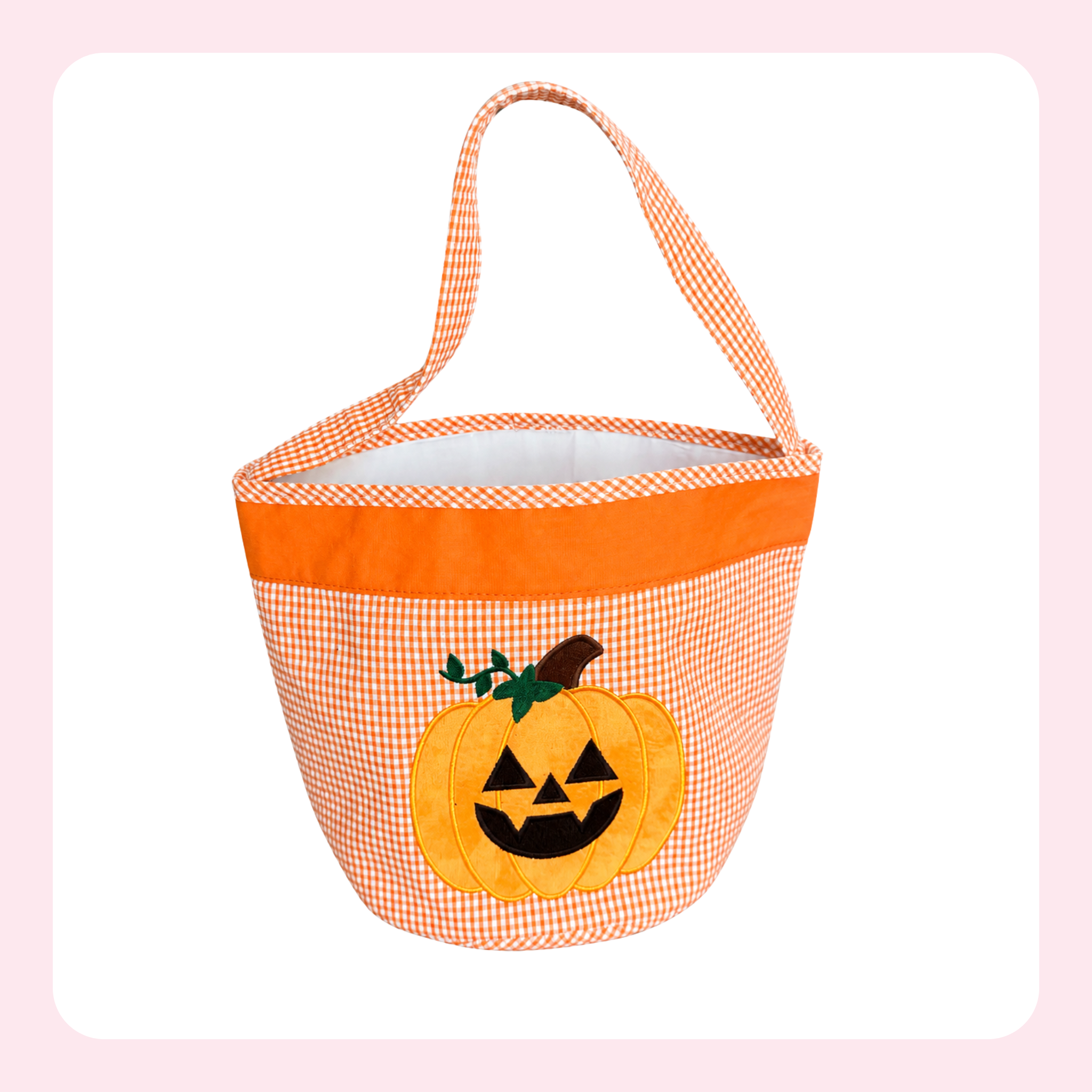 An orange and white gingham bucket bag with a solid orange top band, featuring an applique jack-o'-lantern on the front. The bag has a single shoulder strap and is shown against a white background with a light pink border.