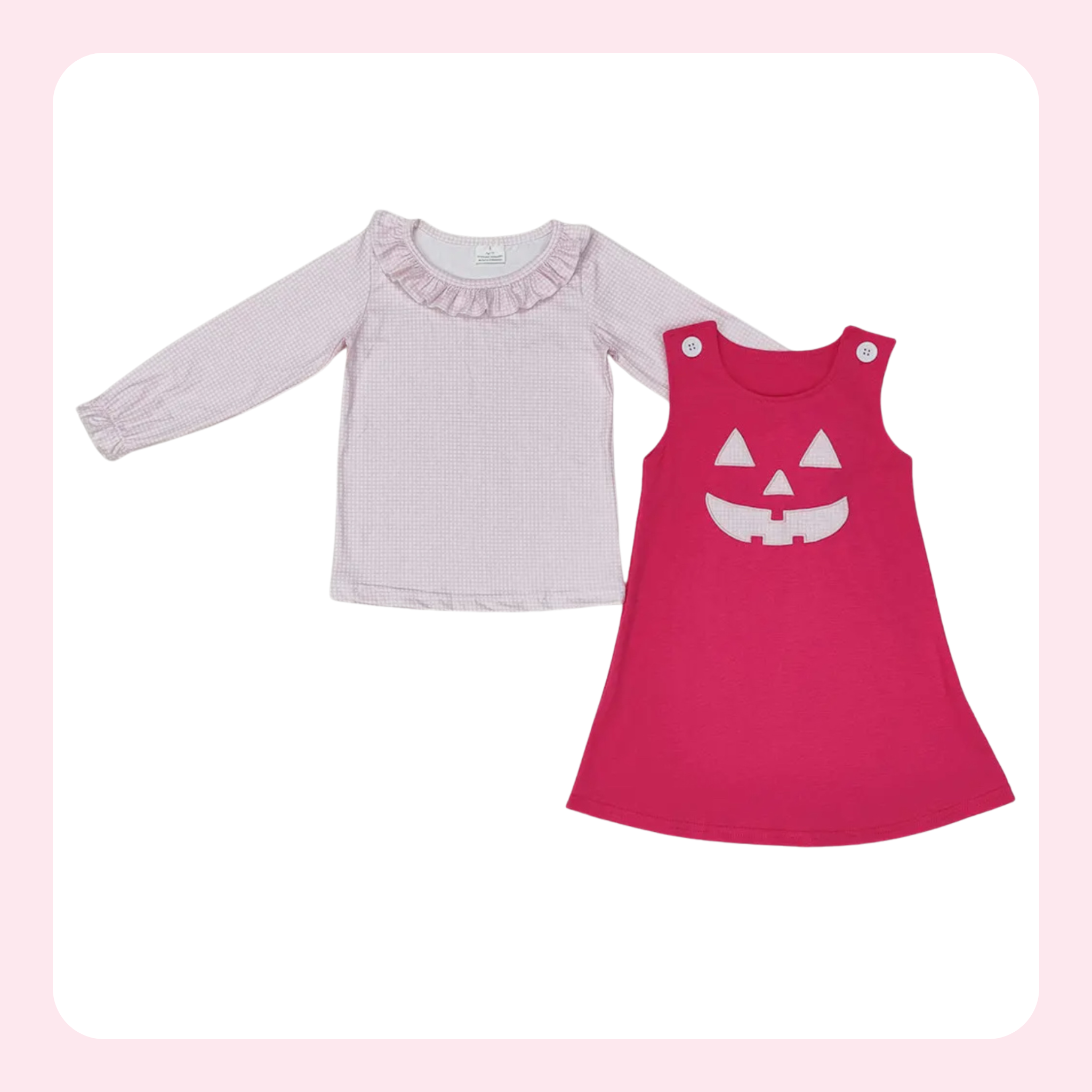 A two-piece baby girl's outfit set featuring a light pink long-sleeve top with a ruffled neckline and a bright pink sleeveless dress with a white jack-o'-lantern face graphic, displayed on a white background with a soft pink border.