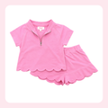 A pink two-piece girls' outfit set featuring a short-sleeve quarter-zip top with a scalloped hem and matching scalloped shorts, displayed on a white background with a light pink border.