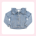 A light blue denim jacket for toddlers, featuring a large ruffled collar, button-up front, and side pockets, shown flat on a white background with a soft pink border.